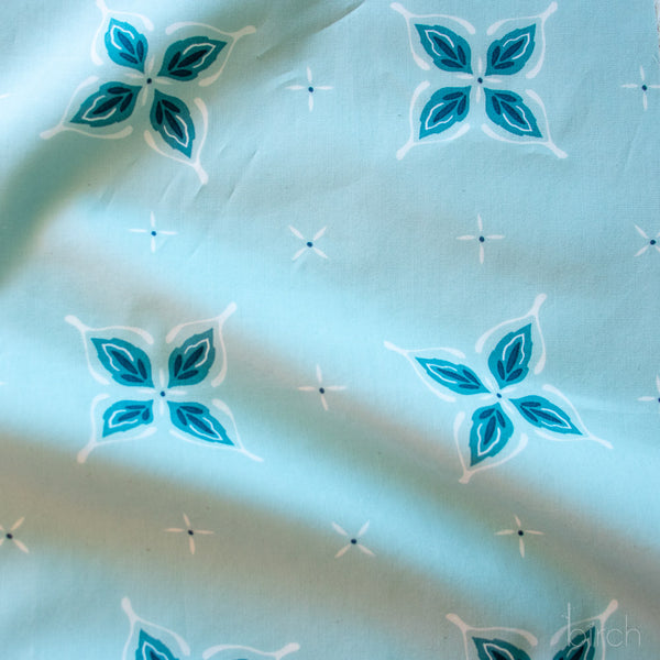 Close-up of fabric with blue and white floral pattern on a light blue background in a bandana style with hidden wishbone motif
