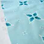 Close-up of fabric with blue and white floral pattern on a light blue background in a bandana style with hidden wishbone motif