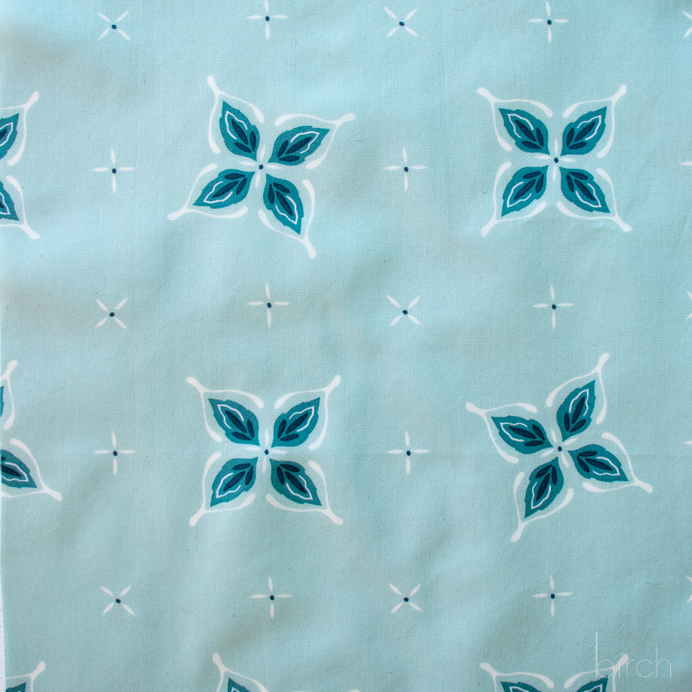 Close-up of fabric with blue and white floral pattern on a light blue background in a bandana style with hidden wishbone motif